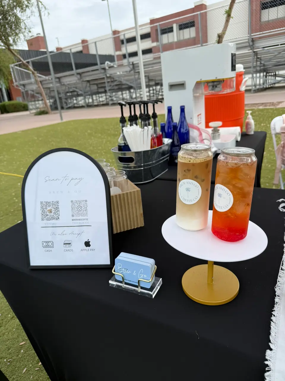 Her bar on a field: two cans on a gold stand, an arched sign and the Brew and Go cloth