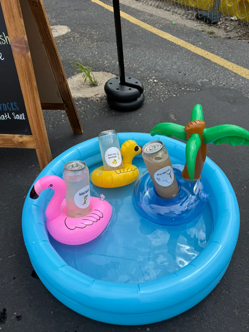 A kiddie pool of canned drinks with an inflatable palm tree, flamingo and duck floats