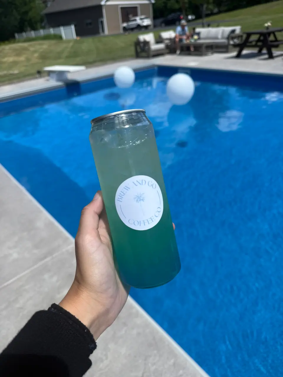 A blue-green drink in a Brew and Go can, held over a swimming pool