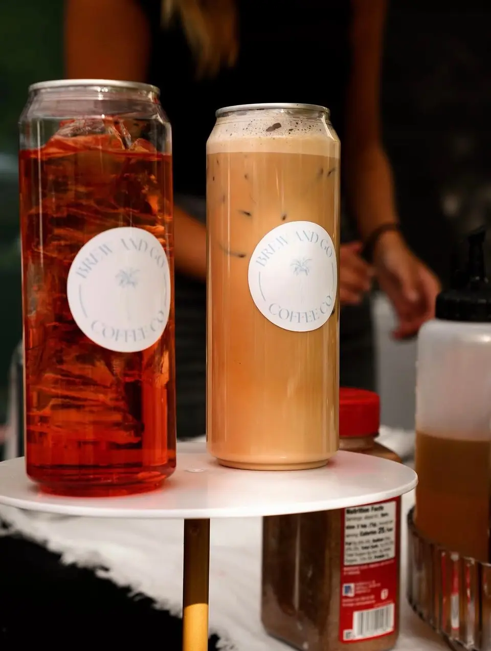An iced tea and an iced latte in Brew and Go cans on a white cake stand