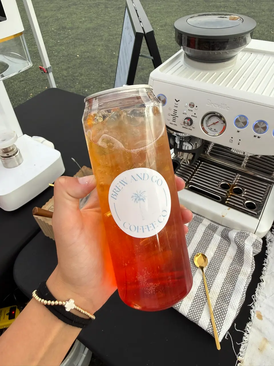 An orange-to-red layered drink in a Brew and Go can, in front of her espresso machine